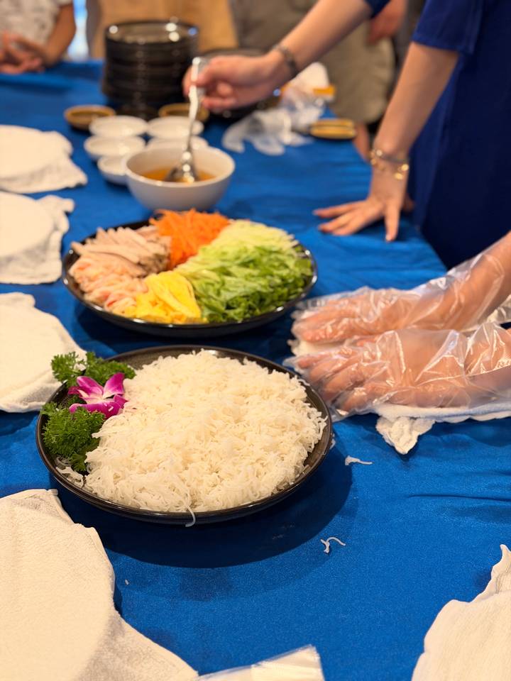 Close-up of ingredients and hands preparing Vietnamese spring rolls on a blue table.