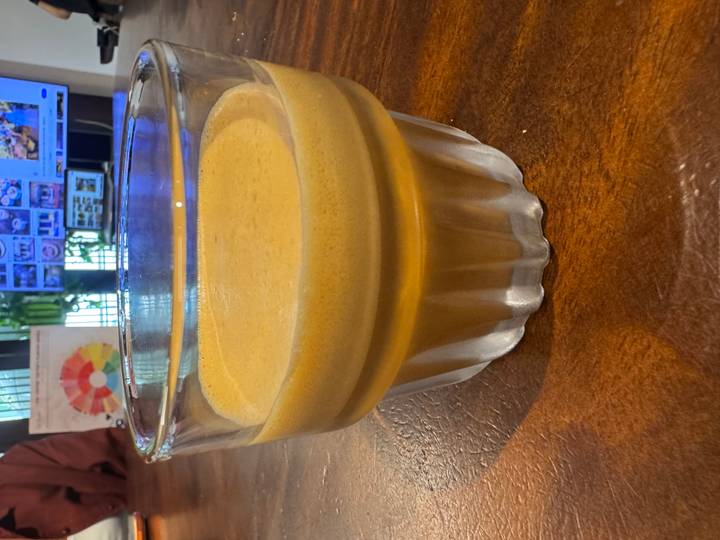 Close-up of a glass containing thick creamy Vietnamese egg coffee on a wooden table.