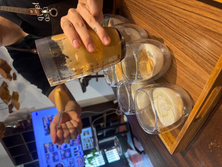 Barista spooning thick coffee foam into double-walled glasses during an egg coffee workshop.