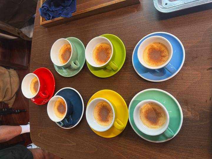 Six colorful espresso cups filled with Vietnamese egg coffee arranged on a wooden table.