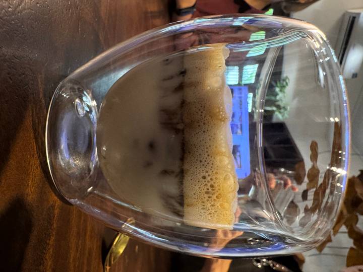 Layered Vietnamese egg coffee showing frothy top and iced milk bottom in a double-walled glass.