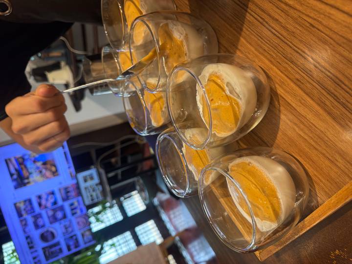 Barista smoothing layers of egg coffee foam over multiple glass cups on a tray.
