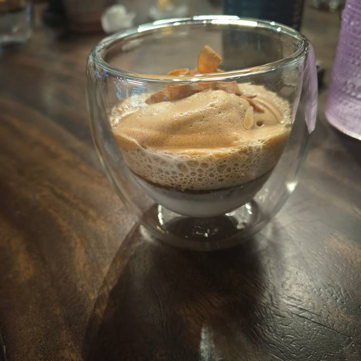 Close-up of a layered Vietnamese egg coffee in a double-walled glass on a wooden table.