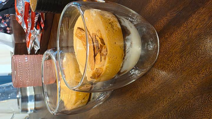 Two servings of Vietnamese egg coffee in clear double-walled glasses placed on a dark wooden table.