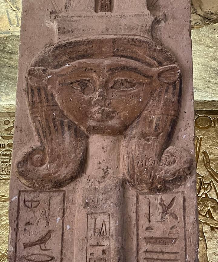 Close-up of an ancient carved relief depicting a feminine face with detailed hair.