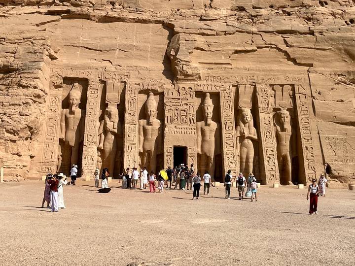 Crowds explore the grand rock-hewn façade of Abu Simbel temple under bright sun.