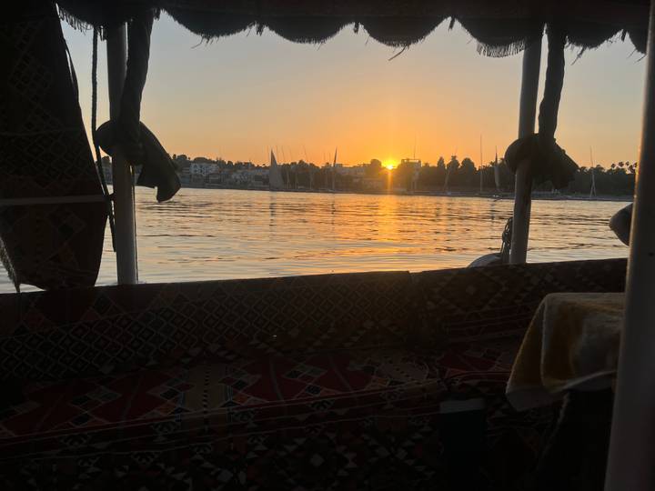 Sun sets behind sailboats on the Nile, viewed from inside a traditional felucca.