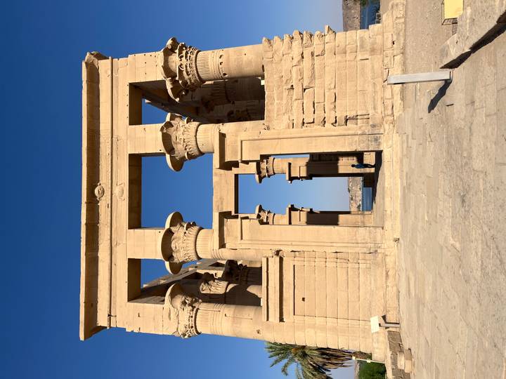Stone gateway with towering lotus-flower capitals at Philae Temple framed by blue sky and water beyond.