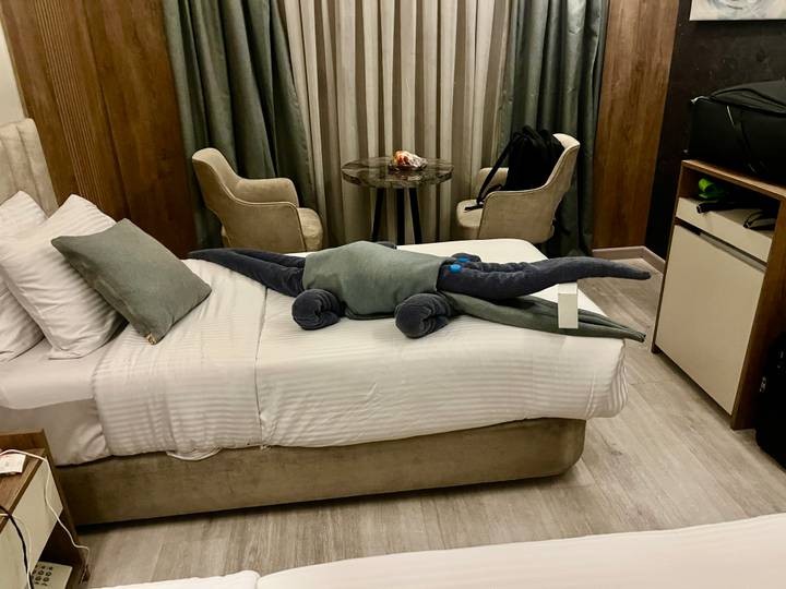 Hotel room bed decorated with a towel folded into a crocodile shape, luggage nearby.