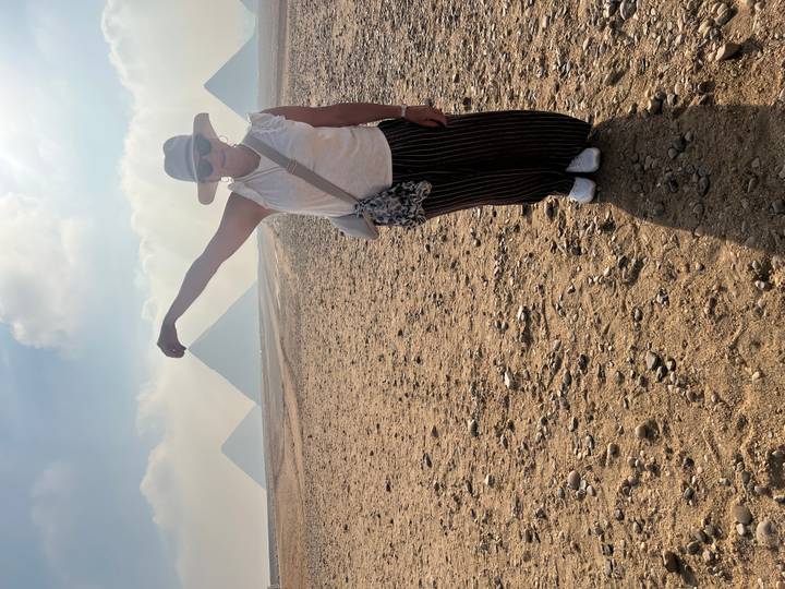 Traveler jokingly 'pinches' distant pyramids while standing on a sandy plain in Giza.