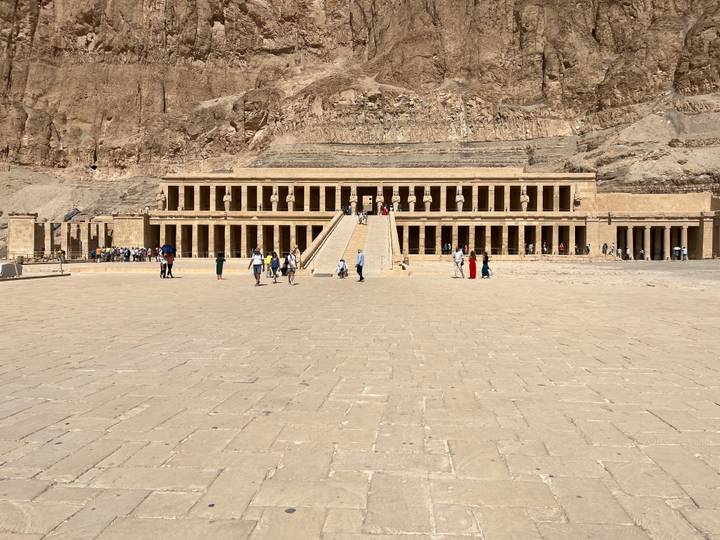 Wide plaza leading to Queen Hatshepsut's terraced mortuary temple with visitors scattered around.