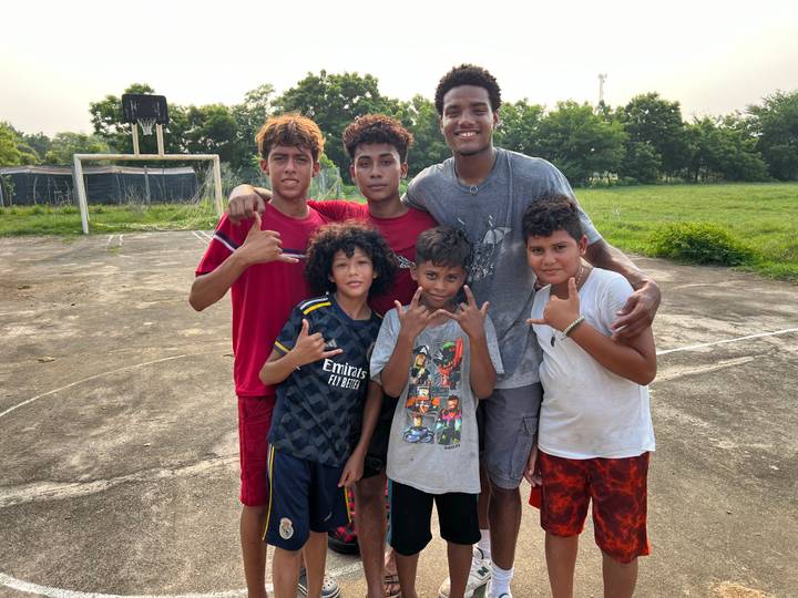 Youthful team poses on an outdoor basketball court with greenery and goals behind.