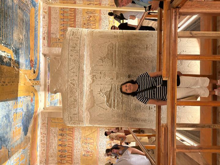 Visitor stands before an intricately carved granite sarcophagus inside a pharaoh's richly painted tomb chamber.