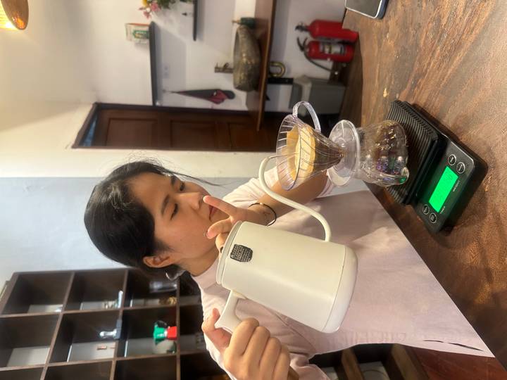 A barista carefully pours hot water over a V60 coffee dripper inside a cosy café.