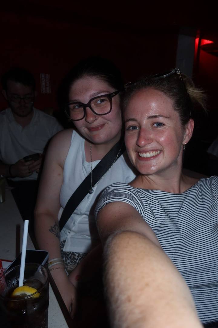 Two young women take a flash selfie in a dimly lit indoor setting.