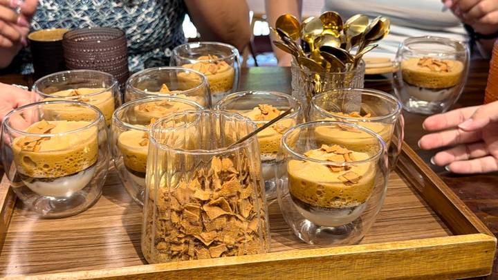 A wooden tray holds multiple glass cups of layered Vietnamese egg coffee garnished with crispy flakes.