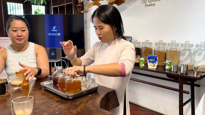 Participants sample different brews while a host explains coffee varieties in a bright roastery.