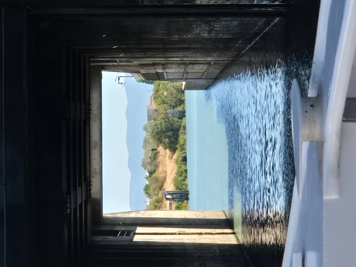 View from a boat inside a concrete lock chamber opening toward a calm river and hills.