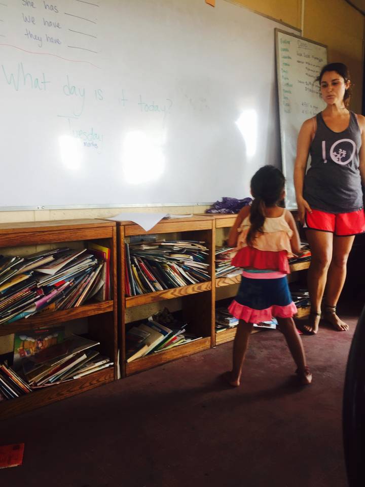 Child standing in front of wooden bookshelves in a classroom.