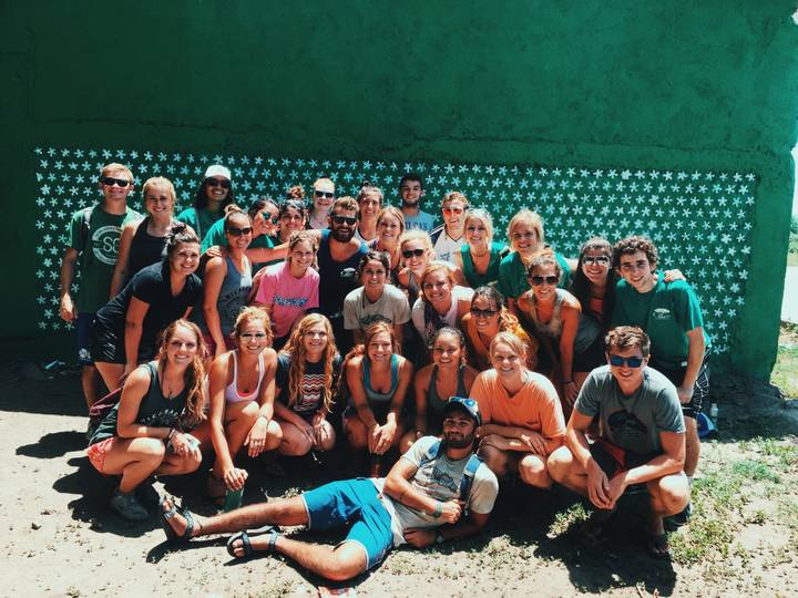 Large group posing in front of a green painted wall.