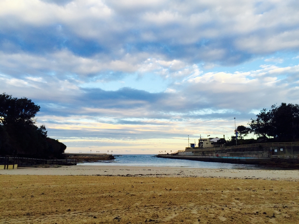 Beach scene with a small cove, sandy beach, and buildings in the distance.