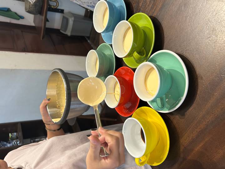 Participant ladles thick egg coffee mixture into colourful cups during a workshop.