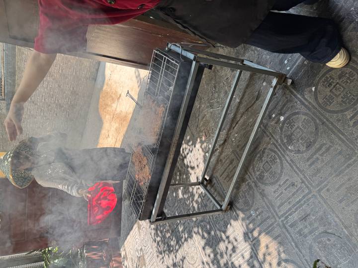 Smoky outdoor charcoal grill with patties and person fanning flames