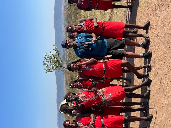 A tourist stands with Maasai tribesmen dressed in traditional red attire on an open plain.