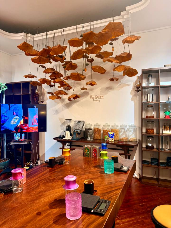 Stylish coffee workshop interior with hanging dried leaves and rows of beans, grinders and jars.