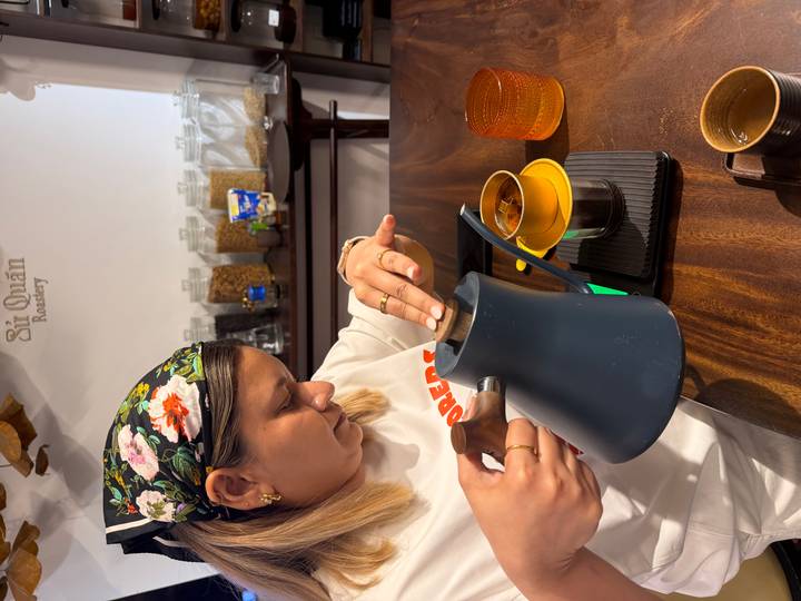Participant carefully pouring hot water from a kettle into a Vietnamese phin filter during a coffee class.