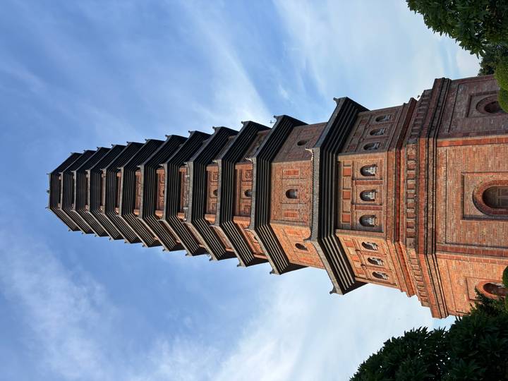 Tall brick pagoda tower with multiple tiers rises against a blue sky at a Vietnamese temple complex.