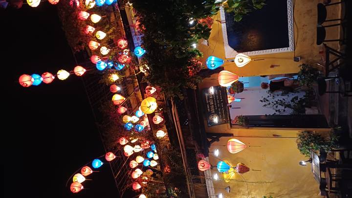 Night scene of a Hoi An café decorated with hanging multicolored lanterns creating a festive glow.