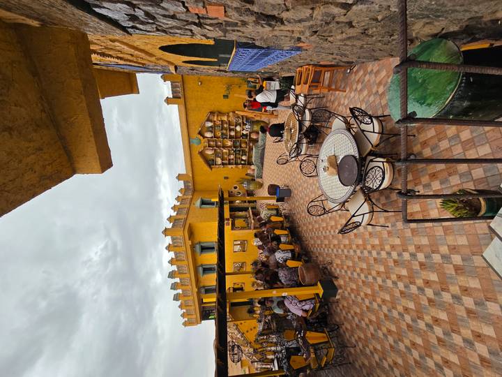 Colorful courtyard café with patterned tiles and yellow adobe walls bustling with guests.