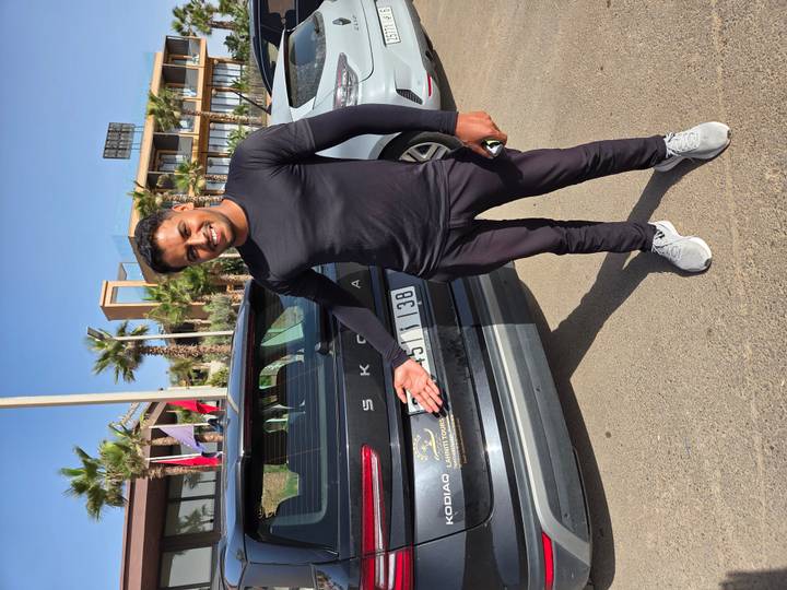 Smiling driver gestures toward a tour vehicle parked under clear blue sky.