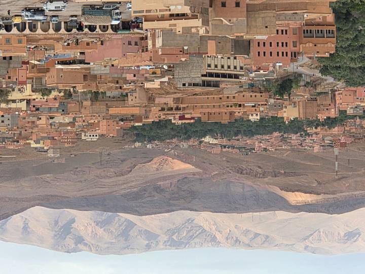 Panoramic view of a desert town surrounded by rugged mountains and date palms.