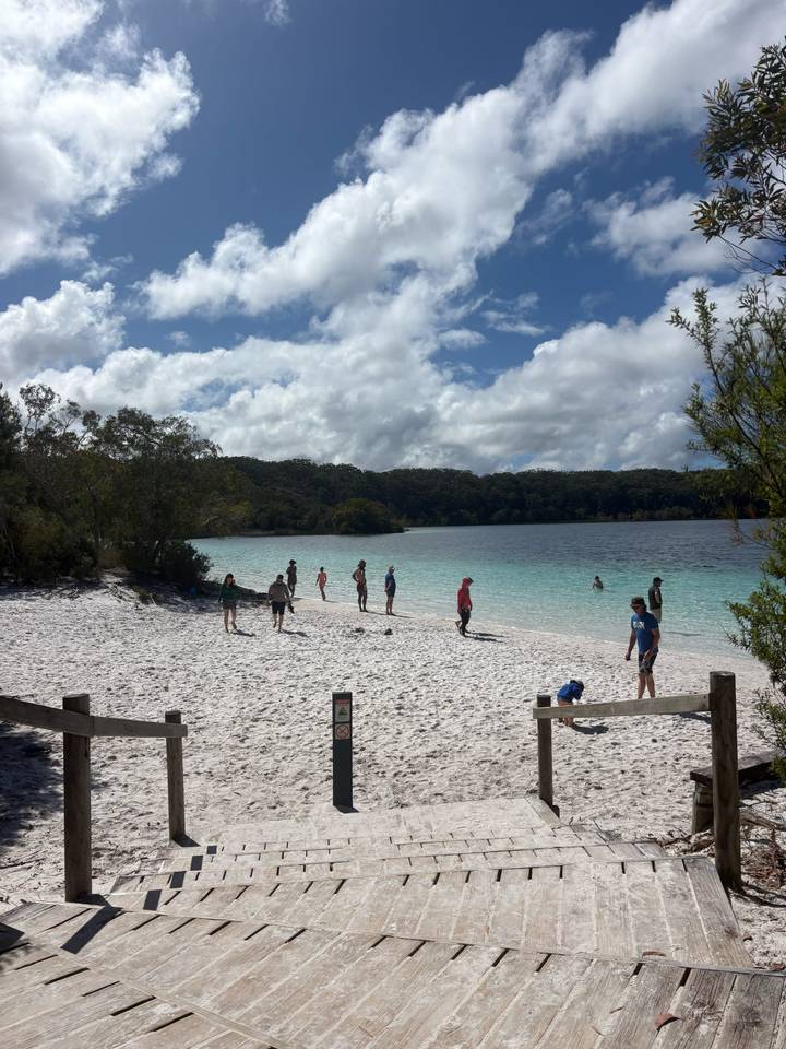 Small group enjoys games on a white-sand lakeshore with turquoise freshwater framed by forest.