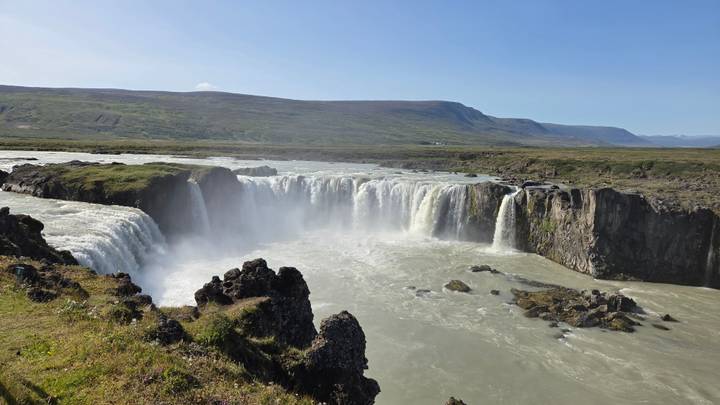 Powerful Godafoss waterfall cascading through rugged cliffs under a clear blue sky.