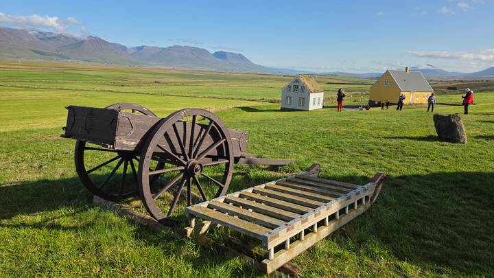 Pastoral Icelandic scene with old wooden cart, turf-roof houses and distant mountains.
