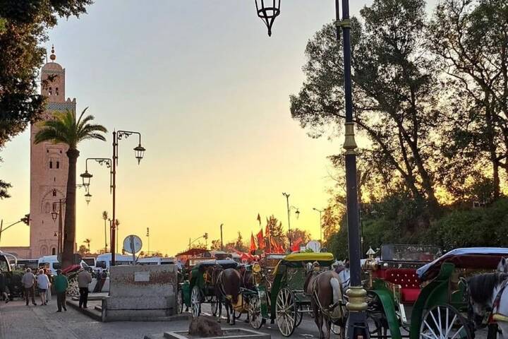 Horse-drawn carriages gather near the Koutoubia Mosque tower at sunset in Marrakech.