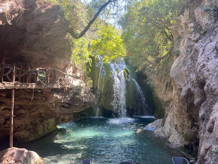 Clear turquoise pool and cascading waterfall shaded by lush greenery inside a rocky gorge.