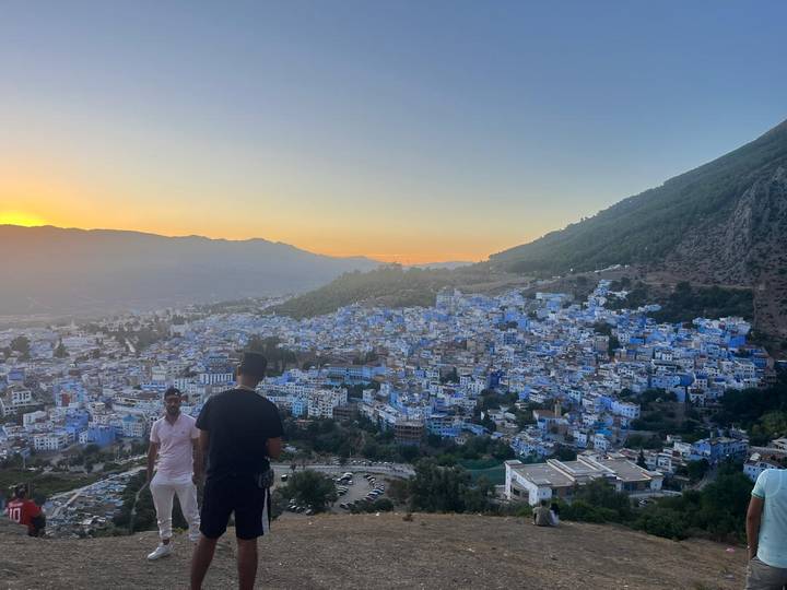 Overlook of Chefchaouen’s blue houses at sunset with visitors enjoying the view in the foreground.
