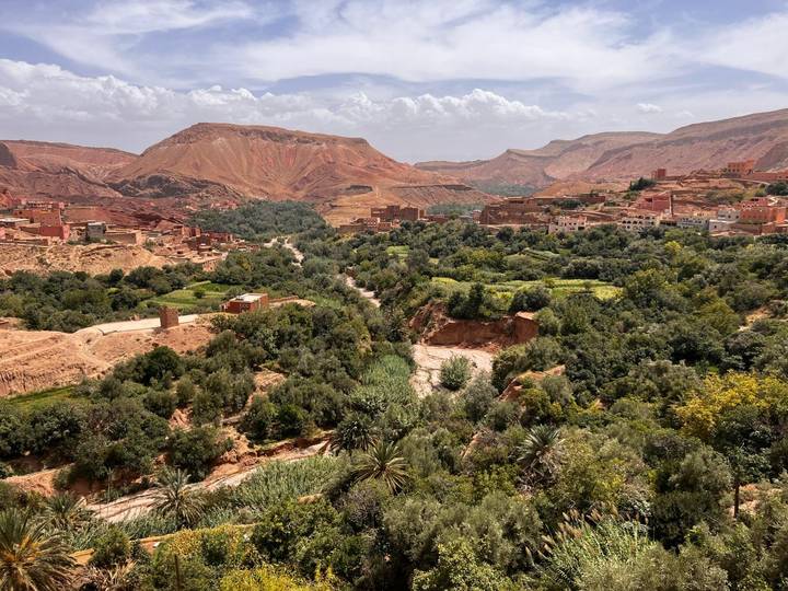 Lush green valley with scattered villages set against red-hued desert hills and distant mountains under a bright sky.