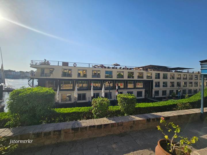 Large Nile cruise ship docked by the riverside with sunbathers relaxing on the upper deck in bright afternoon light.