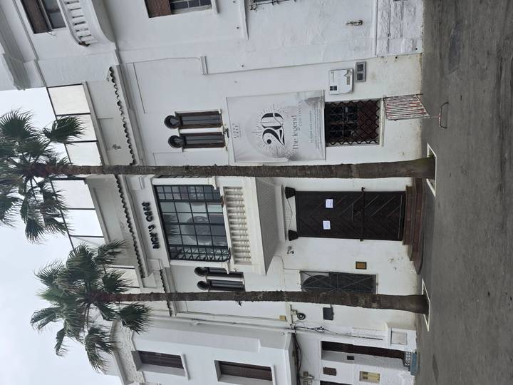 White-washed facade of Rick’s Café with arched windows and palm trees lining the sidewalk.