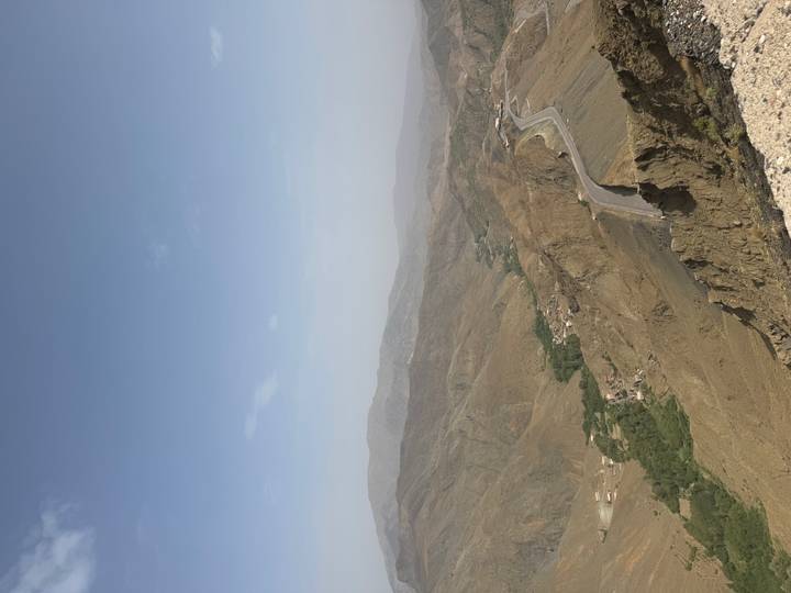 A distant mountain highway winds through rugged brown ridges toward a hazy horizon.