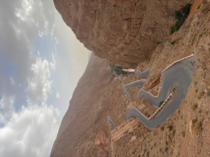 A dramatic switchback road twists through steep canyon walls with scattered clouds overhead.