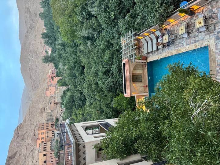 Rooftop pool of a boutique hotel overlooking a lush green valley and desert hillside town in Morocco