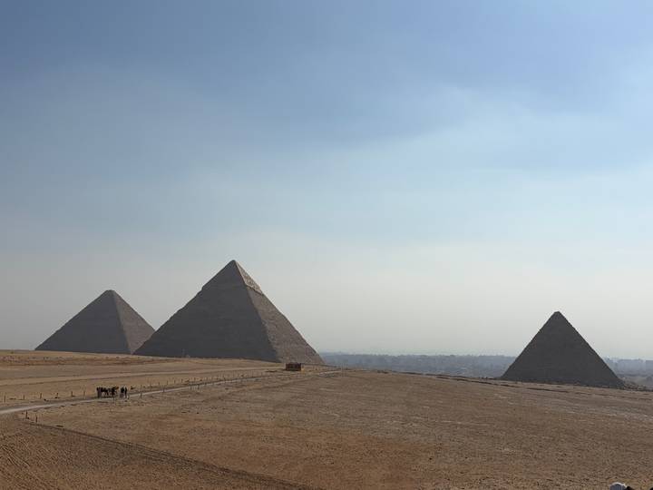 Iconic panorama of the three Great Pyramids rising from the desert plateau against a hazy sky.