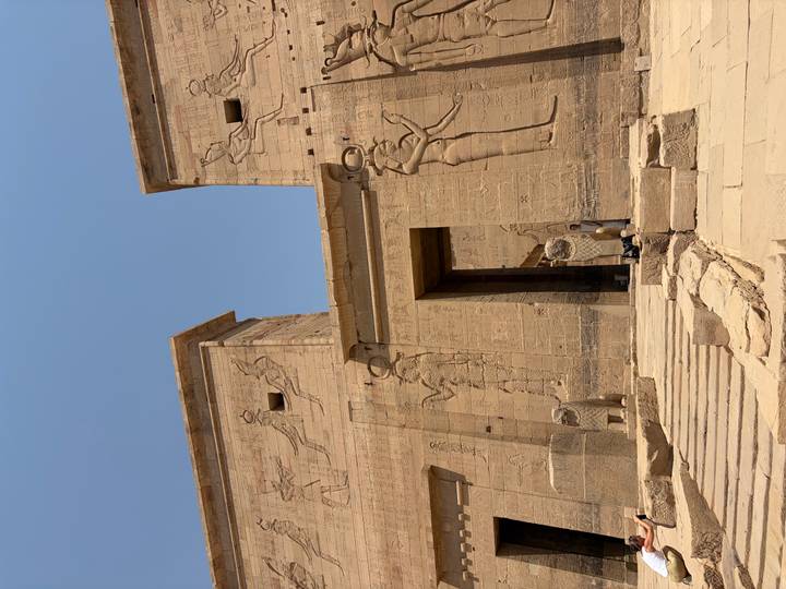 Sand-colored entrance pylons of Philae Temple adorned with carved reliefs beneath a clear blue sky.