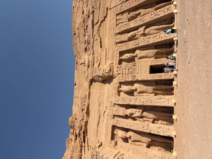 Visitors stand before the rock-cut Small Temple at Abu Simbel featuring colossal statues under a deep blue sky.
